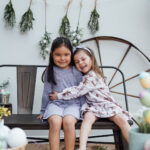 Deux soeurs assises sur un banc, dans un décor de Pâques, se font un câline lors d'une mini-séance photo