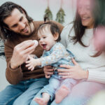 Parents tout sourire avec leur jeune fille sur les genoux qui tente d'attraper un oeuf de Pâques lors d'une mini-séance photo